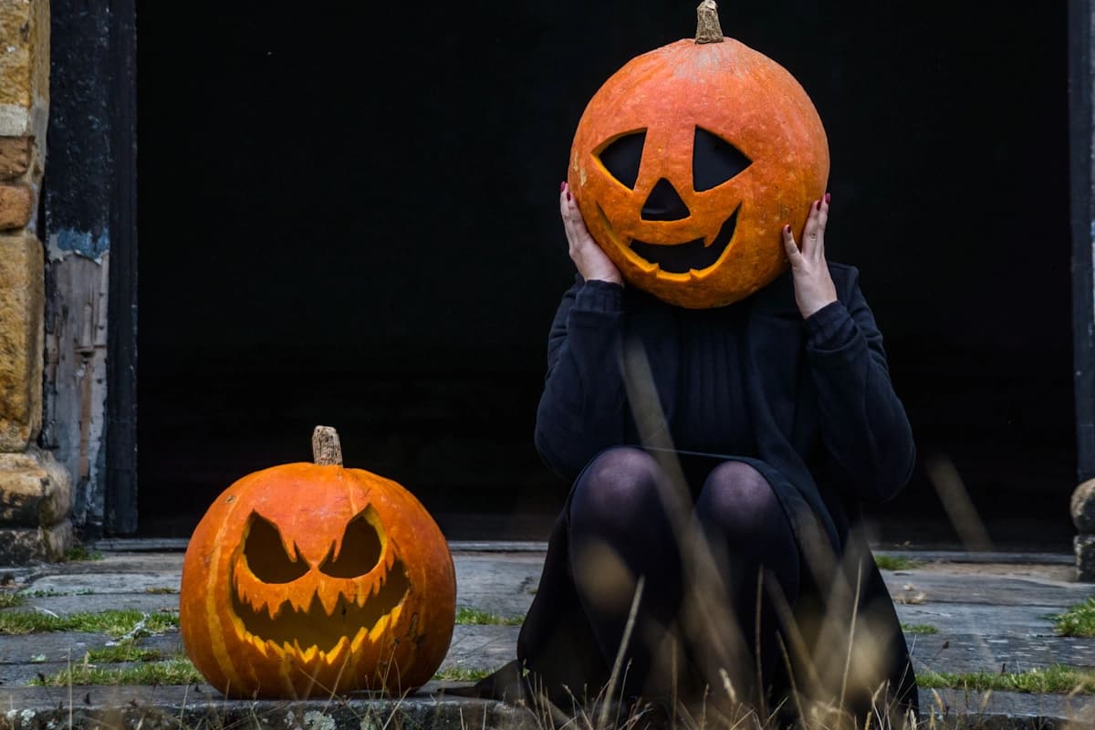 Girl with pumpkin head seating close to the hollowing pumpkin with the monster smile.