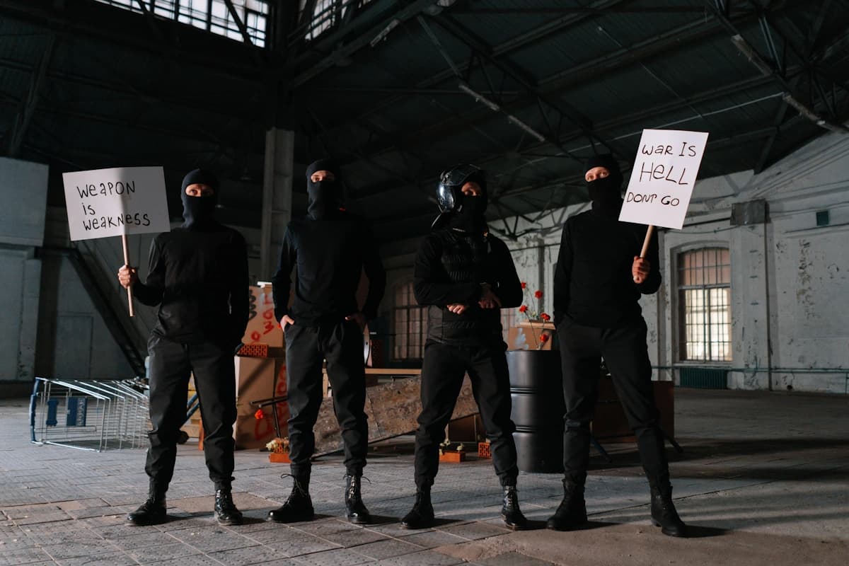 Four people wearing masks and black clothing are inside a dilapidated industrial building.
