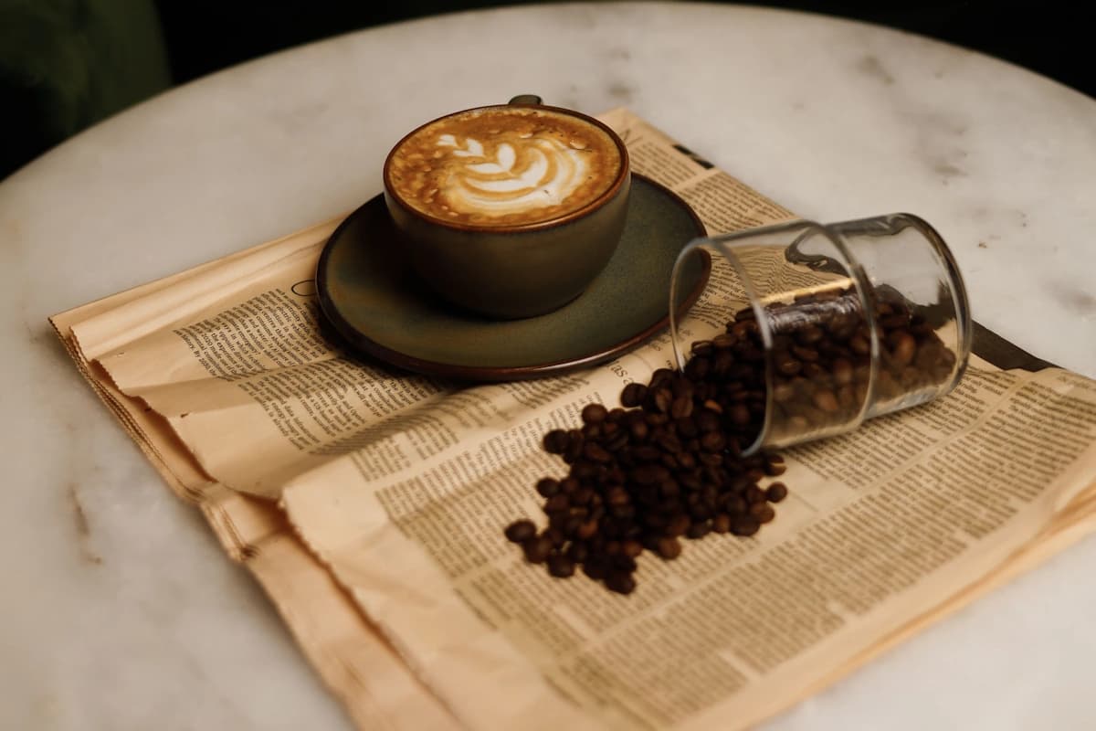 A cup of coffee on a newspaper. Next to it stands a glass containing coffee beans.